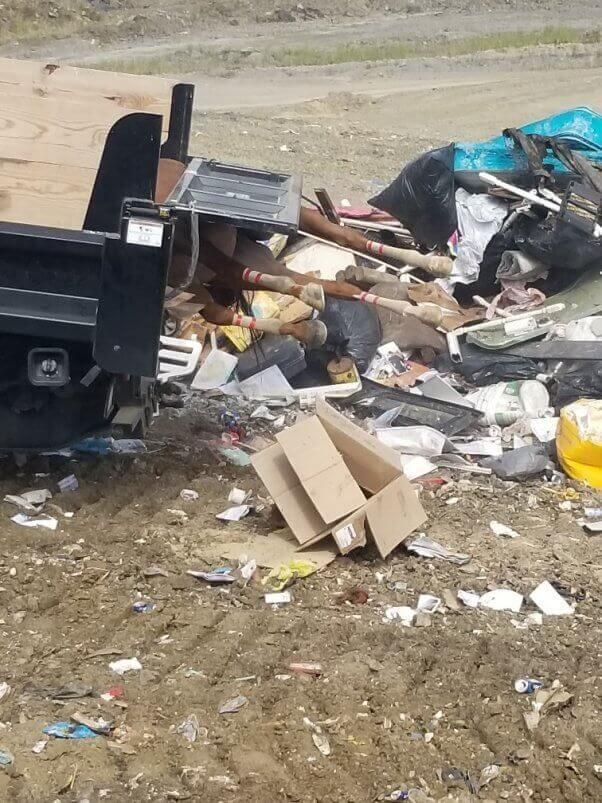 A truck shown dumping trash into a landfill, with four legs of a racehorse poking out of the back of the truck